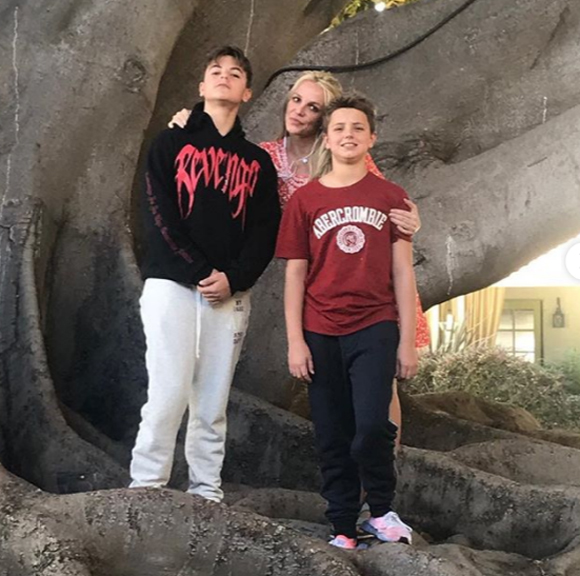 Britney Spears poses with her sons by a tree.